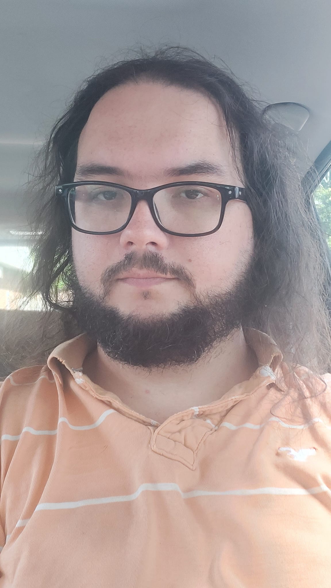 A man with long dark hair sits in a car, he looks sad and tired, photo 1